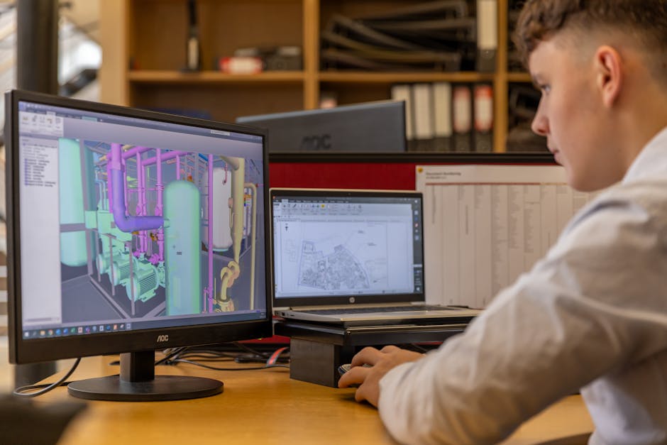 Engineer at a dual-monitor workstation reviewing a 3D CAD model of an industrial process plant