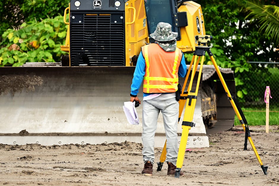 Surveyor operating tripod-mounted scanning equipment at an active construction site