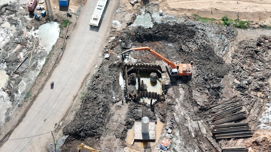 Aerial view of an excavator working muddy terrain at an onshore well pad construction site