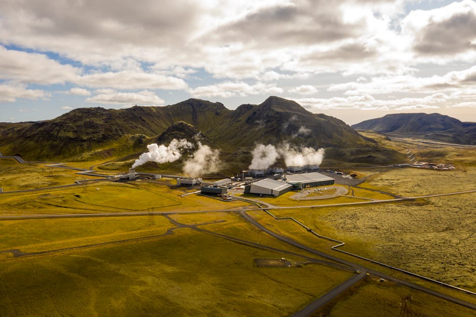 Aerial view of a geothermal power plant with visible steam plumes over a grass field